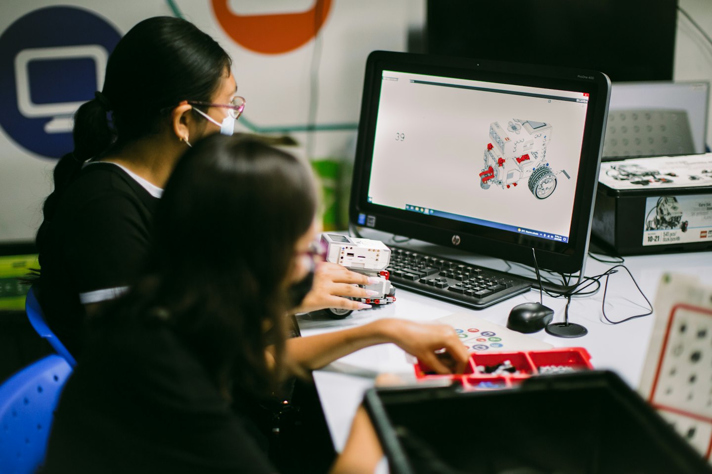 Students wearing masks work on robot parts at a STEM workstation.