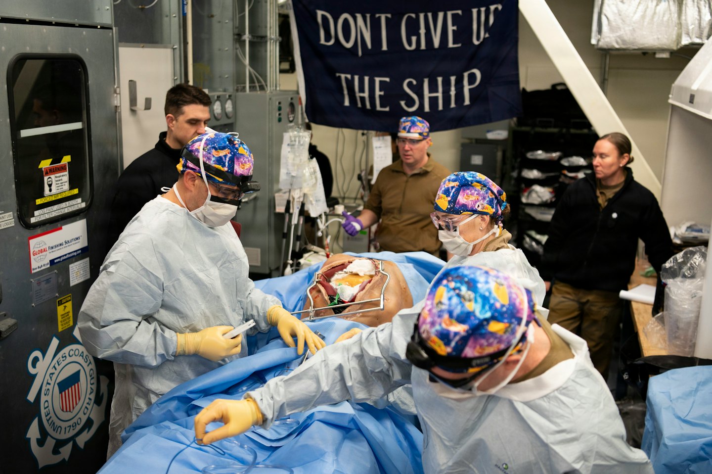 Medical team practices a procedure on a manikin in a ship bay.